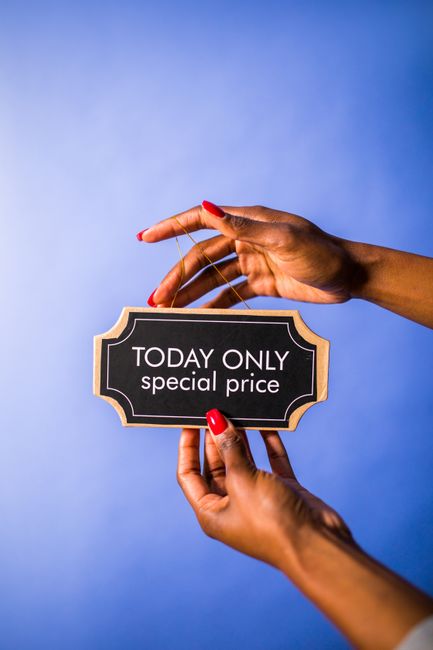 A pair of hands holding a small black and white chalkboard sign with a gold border that reads 'TODAY ONLY special price' against a solid light blue background. The person has neatly manicured nails pa